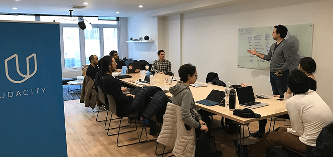 Enterprise learners in a workshop session with an instructor at a whiteboard.